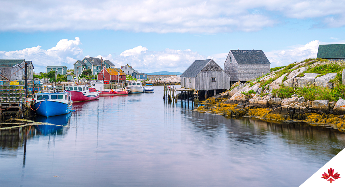 Paysage marin de Peggy’s Cove montrant des bateaux bleus et rouges et des cabanes de bord de mer usées par le temps de chaque côté de la rive.