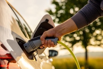 Main insérant un câble d’alimentation dans une voiture électrique blanche pour chargement de manière écologique dans un paysage naturel par une journée ensoleillée.