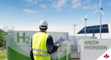 Ingénieur avec une tablette devant une usine d'hydrogène, sous un ciel bleu et ensoleillé.