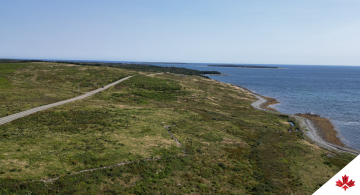 Vue aérienne montrant un paysage verdoyant coupé par une route et l’océan à droite.