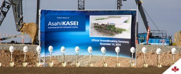 Équipement de chantier à l'arrière-plan et des pelles avec des casques au premier plan. Une bannière bleue annonce le lieu de la cérémonie officielle d'inauguration des travaux d'Asahi Kasei, le 14 novembre 2024. 